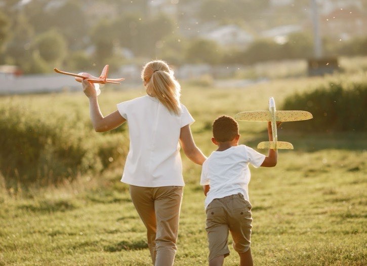 Au pair and child running through a field at sunset