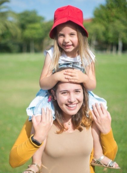 Au pair carrying a child on their shoulders in a park