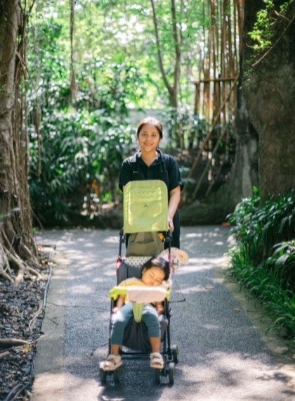 Au pair walking a child in a stroller through a park